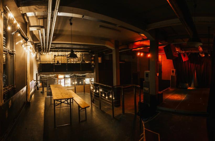 Club Schilli interior, string lights over a wooden bench and a red-lit stage